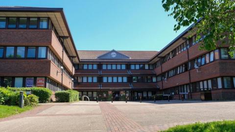 Gateshead Civic Centre. The three-storey building is red brick with rows of windows at each level. A clock has been installed above the entrance.