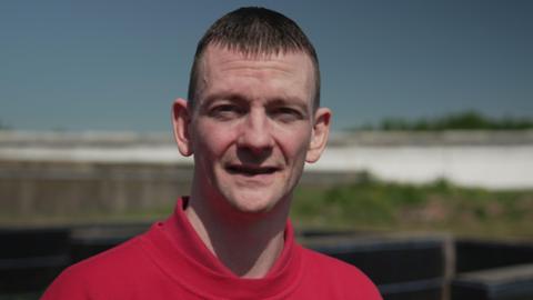A close-up outdoor portrait of a man wearing a plain red sweatshirt.
