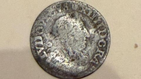 The coin is silver and has Roman numerals and a figurehead. The coin is slightly worn.