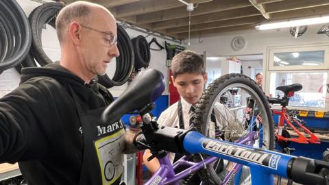 A man and a youth working on a bicycle in a repair shop 