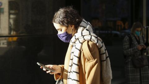 A woman wearing a protective mask reads her phone in New York