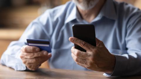 Stock image of man holding credit card and phone