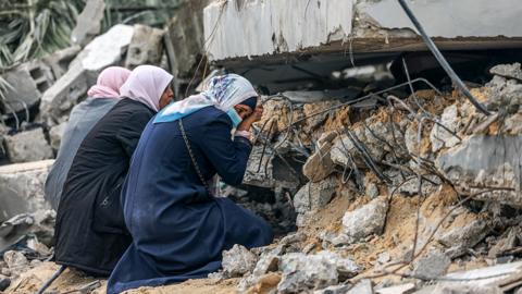 Palestinian women cry where a relative is believed to be trapped in debris following Israeli bombardment in Rafah in the southern Gaza Strip on December 21, 2023