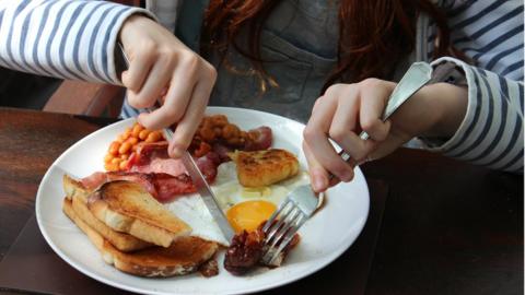 Girl eating fried breakfast of eggs, beans, sausages