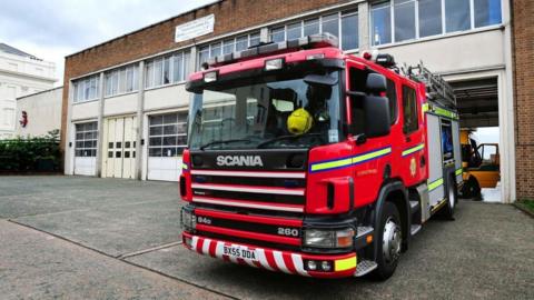 Warwickshire Fire & Rescue’s headquarters in Leamington Spa: a brick building with lots of windows and white panelling. A fire engine is parked outside.