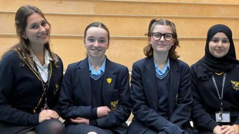 Four pupils in navy blue uniform ar sat on a school bench. 