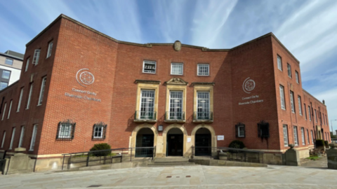 The Riverside Chambers is pictured. It is a large red-brick building with three archways.