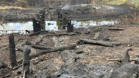 A low angle shot of a bridge devastated by a fire where the fixtures are the only parts still standing, the rest is burnt black