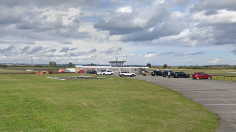 Cars parked near an aviation tower, which is surrounded by green grass. 