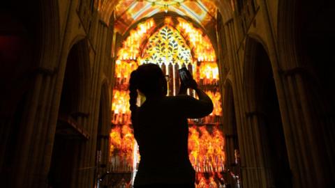 A silhouette of a woman with a phone, in front of the art installation depicting York Minster on fire