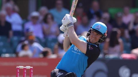 Ed Pollock has his bat in the air after hitting the ball in a match.