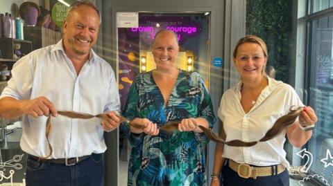 Ruth Tripp with Phil Brace and Wendy Tarplee-Morris (right) from The Little Princess Trust. They are holding Ms Tripp's brown hair which has been cut off