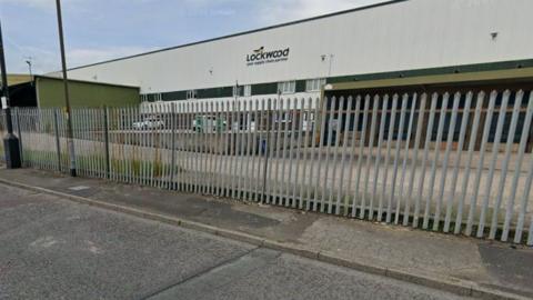 The front of a premises behind a metal fence on an industrial estate. The name 'Lockwood' is emblazoned across the front.