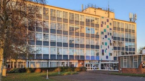 A five-storey building with many windows and a welcome sign outside on the ground floor.