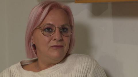 Danielle has shoulder length pink hair and is wearing light rimmed glasses and a white knitted jumper