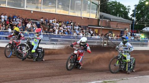 Four speedway riders race around the track as the Oxford crowd watches on.