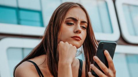 Photograph of young woman looking at mobile phone with serious expression on her face.