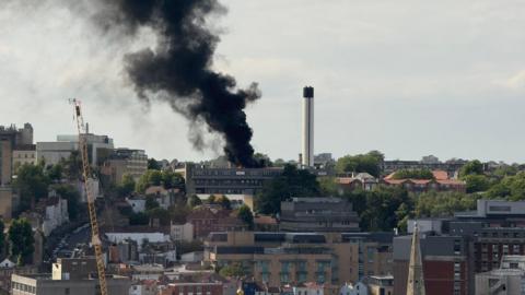 A skyline shot of Bristol showing the fire at St Michael's Hospital. A thick black smoke plume can be seen coming from the roof of the building. The Cotham area of the city can be seen in the distance.