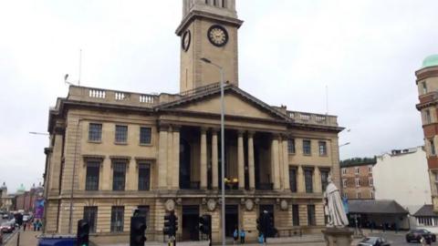 The Hull Guildhall. It is a three-storey light stone building with columns on the front and a clock tower in the middle.