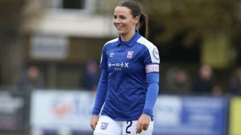 Ipswich Town Women's defender Maria Boswell on pitch, wearing her blue and white ITFC kit. She is wearing the captain's armband.