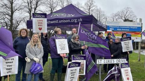 Staff holding signs and flags with a lot of purple outside a hospital sign