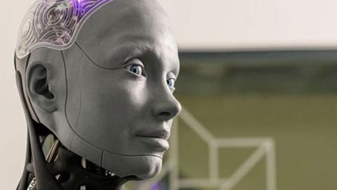 A robot with a grey human face looks to the side, with a see through brain that lights up