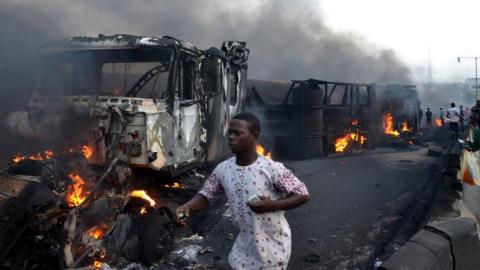 Passersby walk amid burned cars after an oil tanker exploded on a highway in Lagos, 28 June 2018