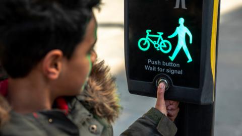 Young boy presses pedestrian light illuminating the green man