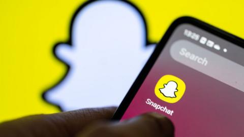 Stock image shows the Snapchat app on a smartphone against a backdrop of the the platform's logo