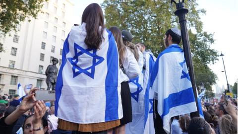 People wrapped in the Israeli flag take part in a vigil outside Downing Street