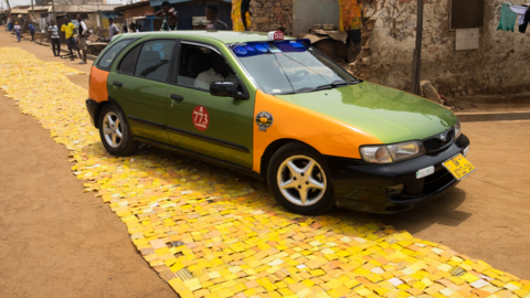 A car on yellow tapestry created by artist Serge Attukwei Clottey on a road in La - Accra, Ghana