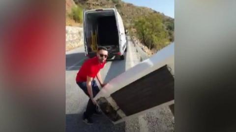 Man preparing to throw fridge over cliff