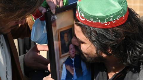 A supporter of the Pakistan Tehreek-e-Insaf (PTI) kisses a portrait of jailed former prime minister and party leader Imran Khan during a protest outside a temporary election commission office in Peshawar on February 10, 2024,