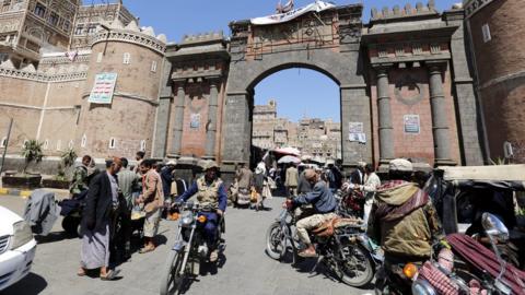 Yemenis walk and ride mopeds through the main gate of the old city ahead of a UN-announced ceasefire, in the old city of Sanaa