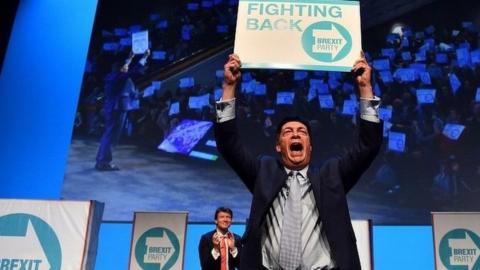 Nigel Farage holding poster aloft at Brexit Party rally