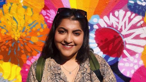 Sarah Island standing in front of a mural of colourful flowers