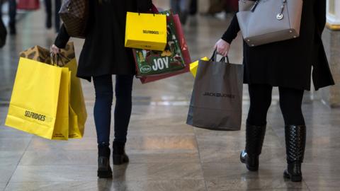 Shoppers carry bags containing purchases from Selfridges and Jack Jones stores through the Trafford Centre shopping mall.