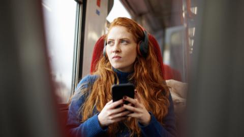 Woman on a bus listening to audio from a phone on headphones