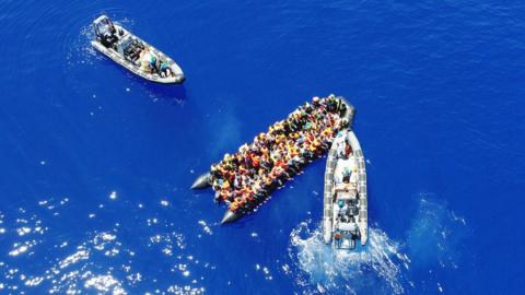 Two Irish naval boats are seen attending to migrants stranded on an inflatable boat