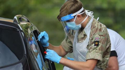 man in army uniform wearing mask, gloves and visor doing swab through car window