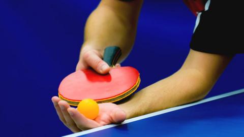Hand holding table tennis bat and ball. File photo