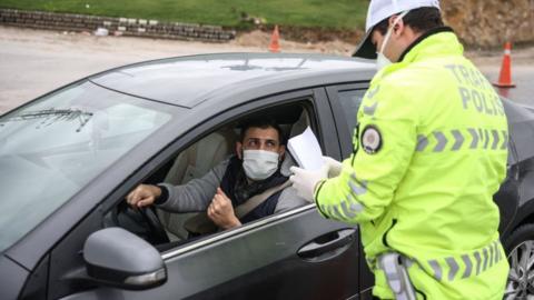 A man wearing a face mask has paper checked by a police officer outside of his vehicle