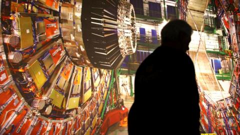 A worker walks past a giant photograph of the Large Hadron Collider