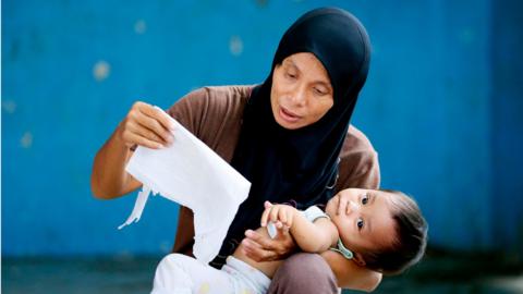 A Filipino Muslim mother cuddles her baby as she checks her name and polling precinct on a list, on Sunday, in Davao city