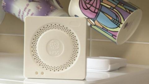 Close-up of small, white electronic box standing in front of some coloured mugs in a kitchen