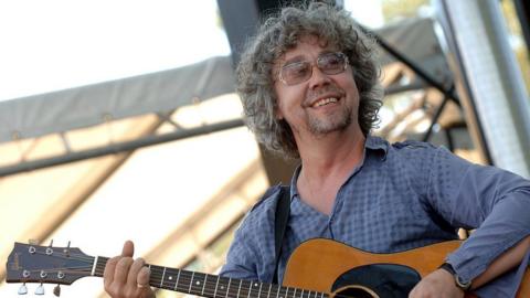 Musician Karl Wallinger seen on stage holding a left-handed acoustic guitar