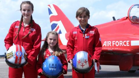 Blue Peter competition winners in front of an RAF aircraft holding helmets with their winning designs.