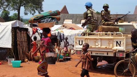 A woman and a child walk past UN peacekeepers from Gabon patrolling the Central African Republic town of Bria on June 12, 2017