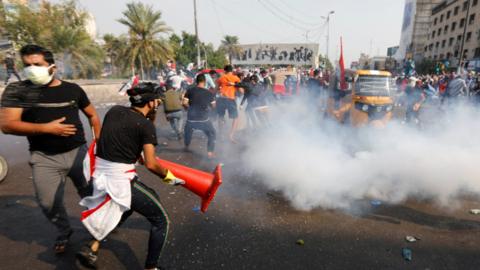 Anti-government protesters run from a tear-gas canister during a protest in Tahrir Square, Baghdad (28 October 2019)