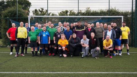 Roughly three dozen football players standing for a group photo in front of a goal